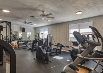 A gym room featuring various exercise equipment and a ceiling fan for ventilation and comfort during workouts.