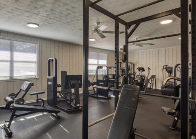 A gym room featuring various exercise equipment and large mirrors reflecting the workout space.